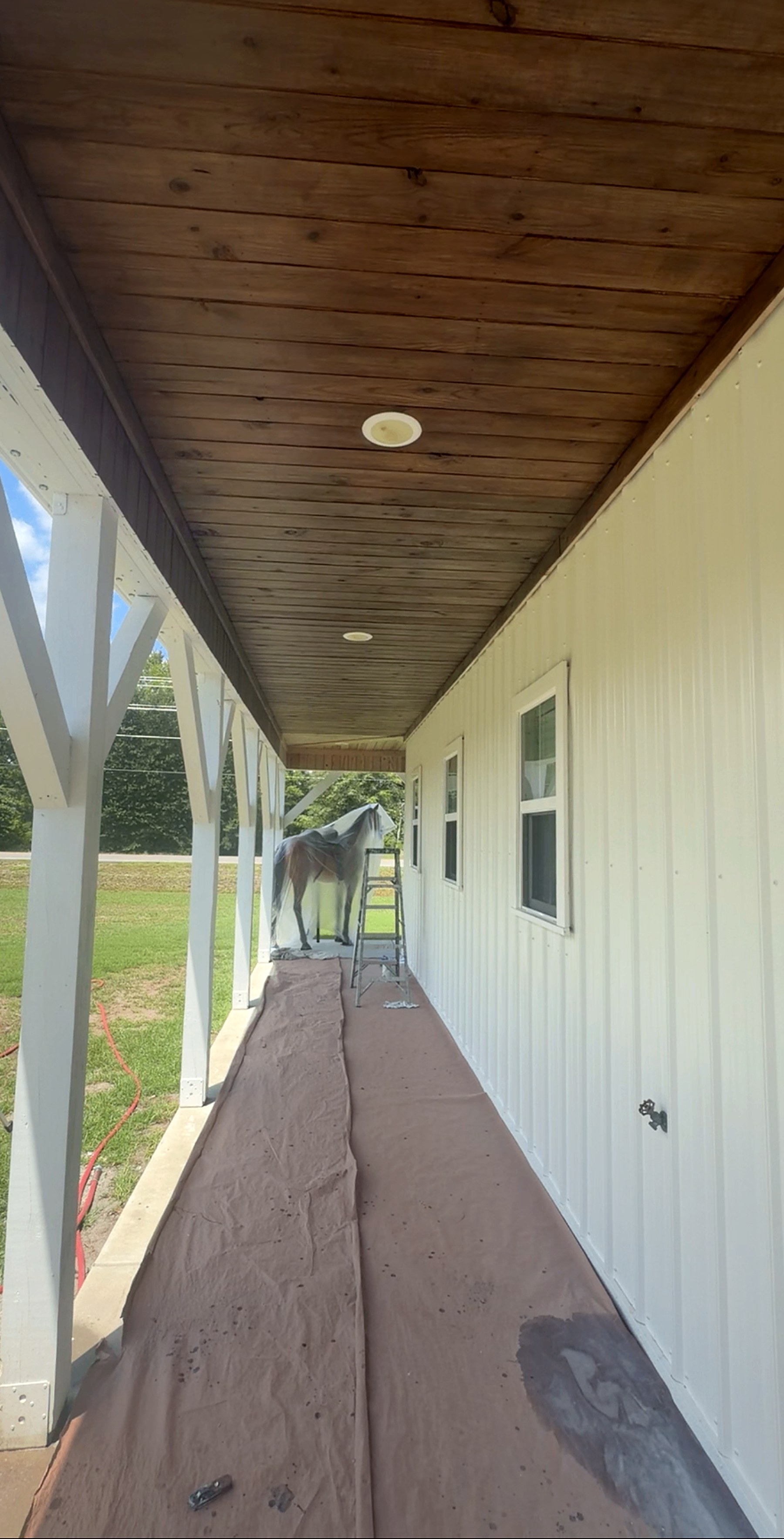 Covered porch with a freshly stained wood ceiling and white posts, drop cloths still down