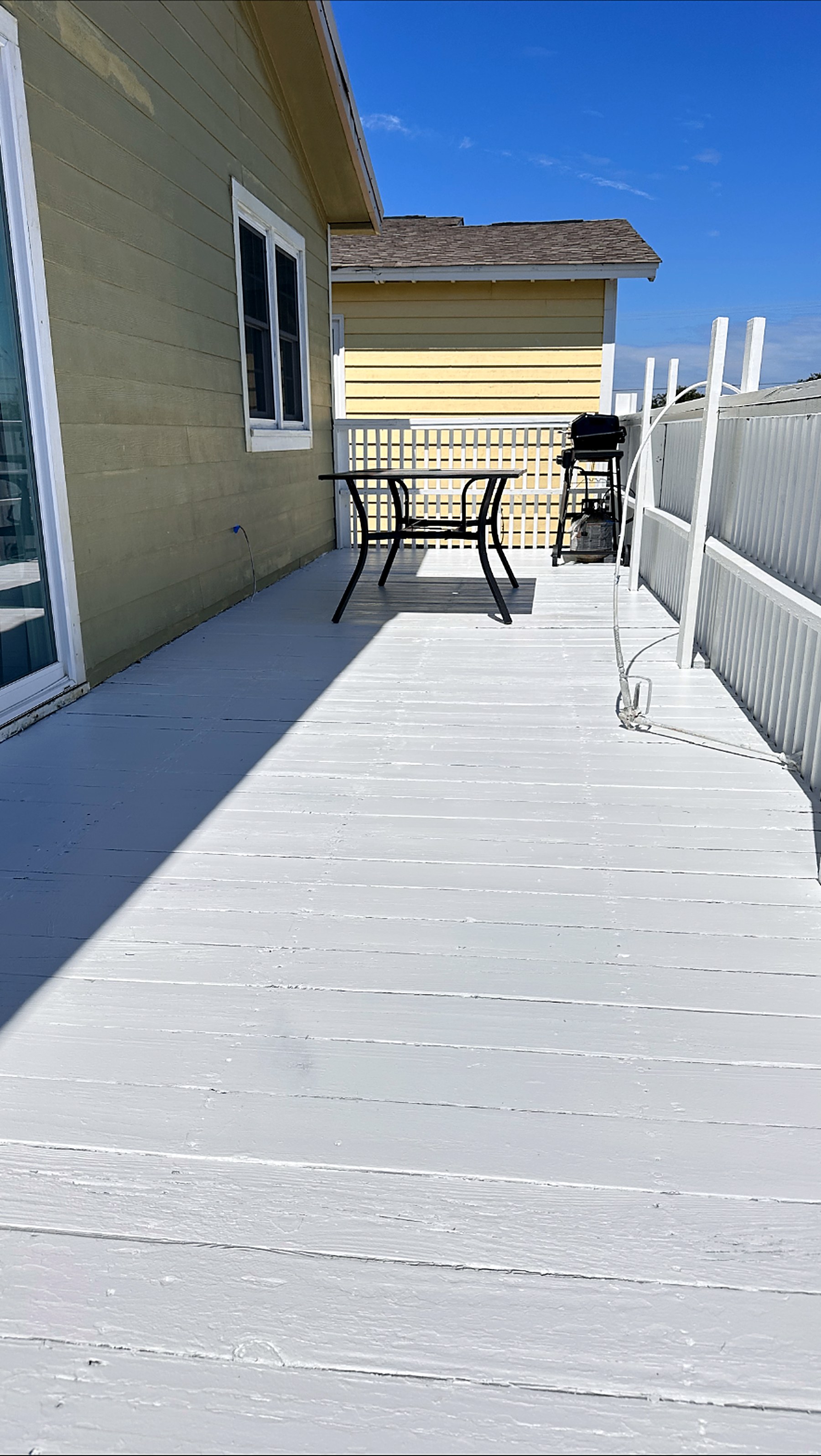 Wide sun-lit deck with newly painted white deck boards beside olive and yellow siding