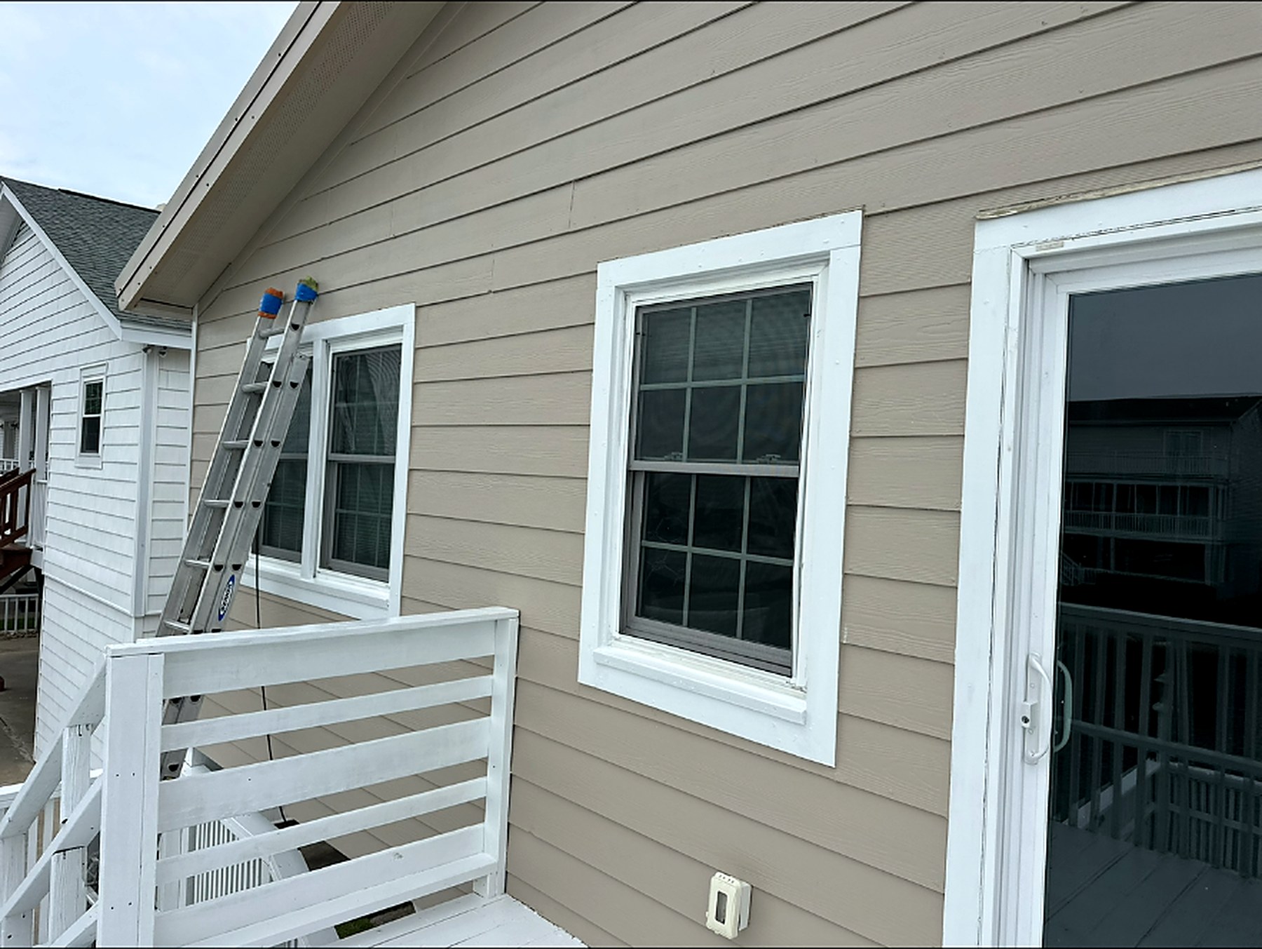 Exterior siding repainted in greige with bright white window trim and deck railing